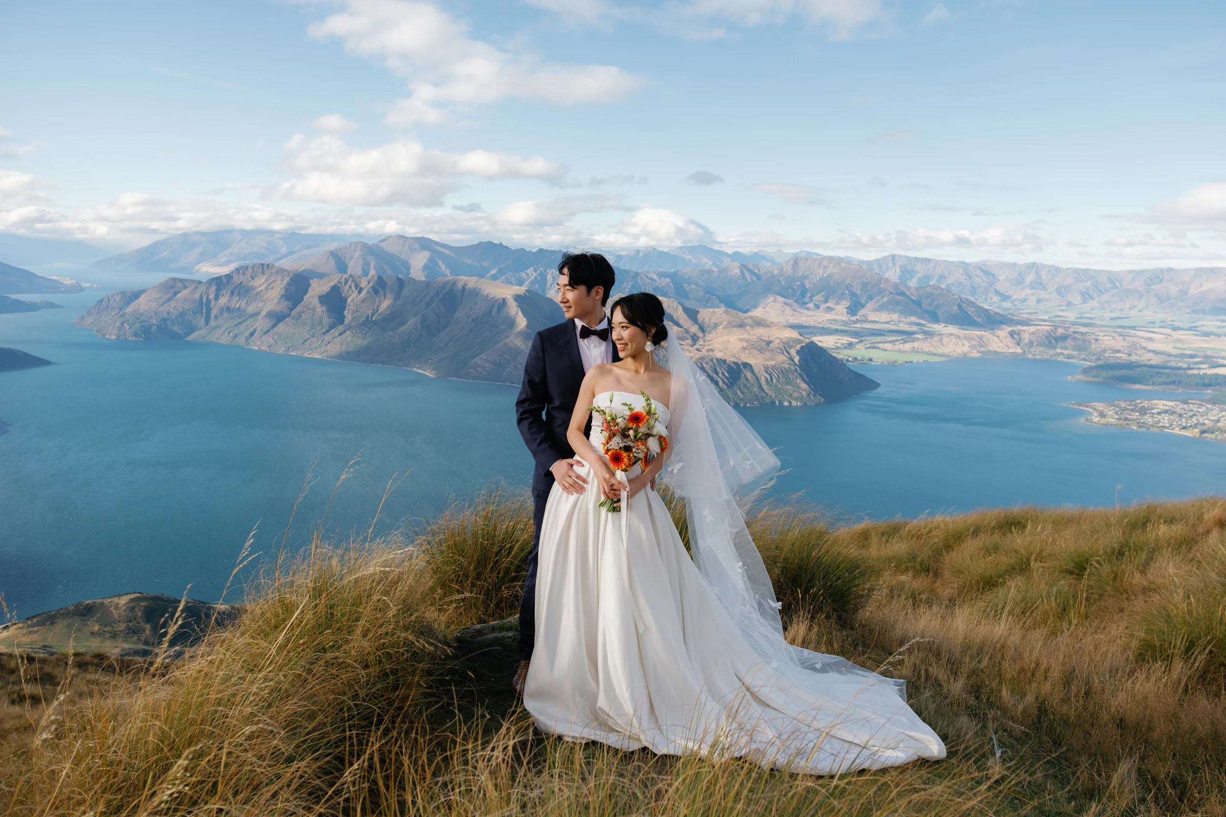 The bride and groom embracing in a lakeside meadow