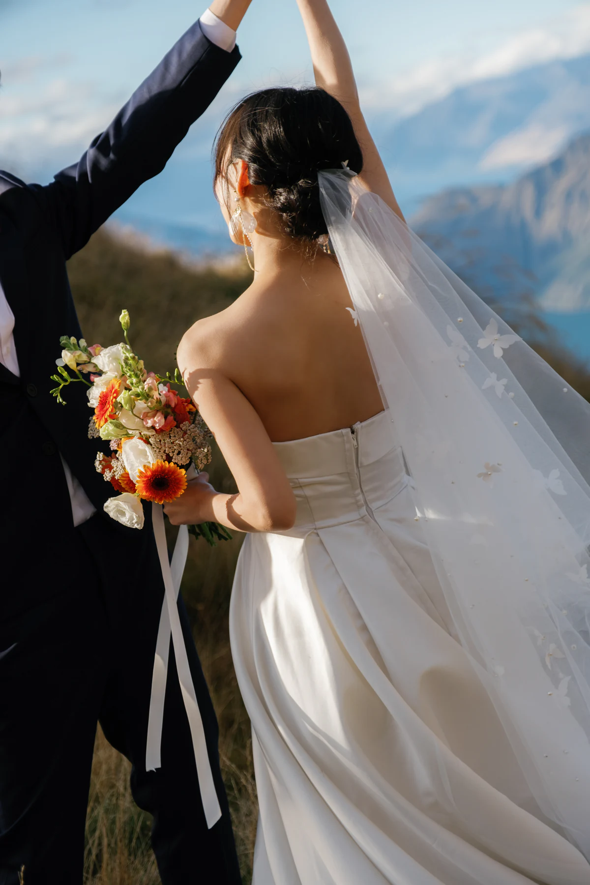 The bride holding a bouquet as the groom raises her hand