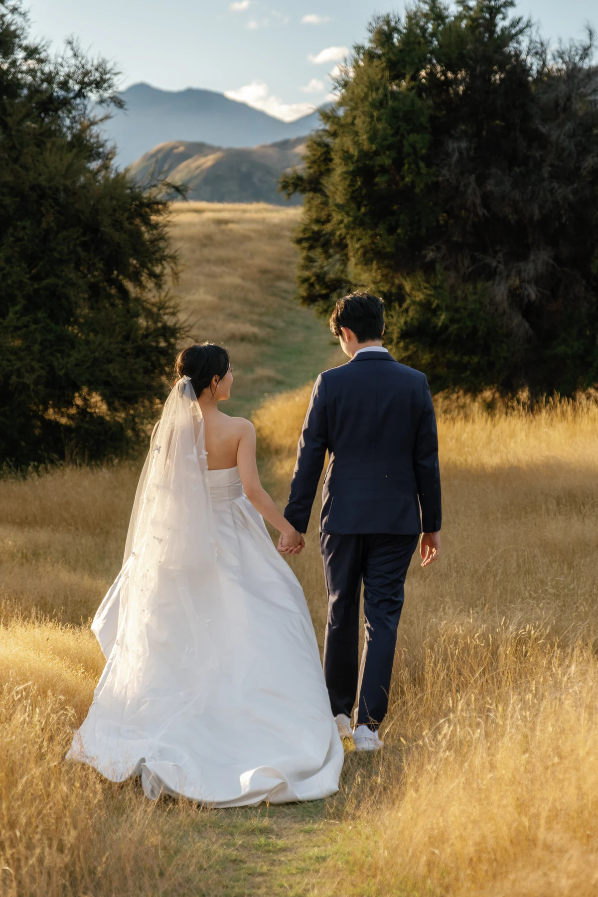 The bride and groom walking hand in hand through a golden meadow