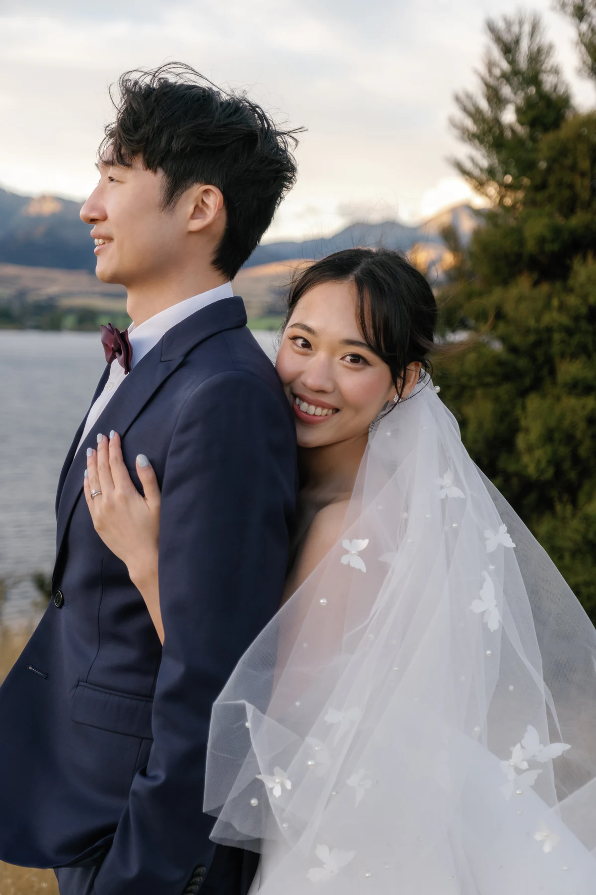 The bride leaning against the groom from behind and smiling toward the camera