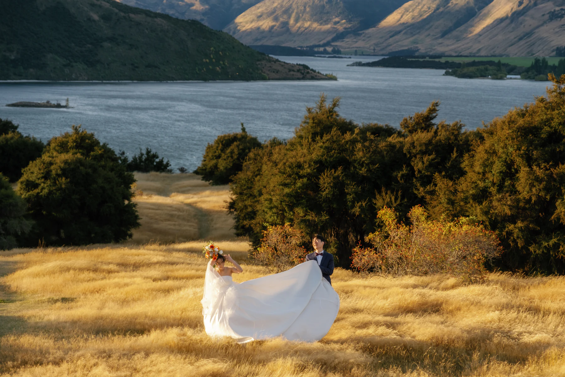 The groom lifting the bride's white train in a golden meadow